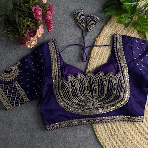 May include: A dark purple blouse with gold embellishments. The blouse features a lotus flower design on the front, with intricate beadwork and sequins. The sleeves and neckline are also adorned with gold detailing. The blouse is a traditional garment.