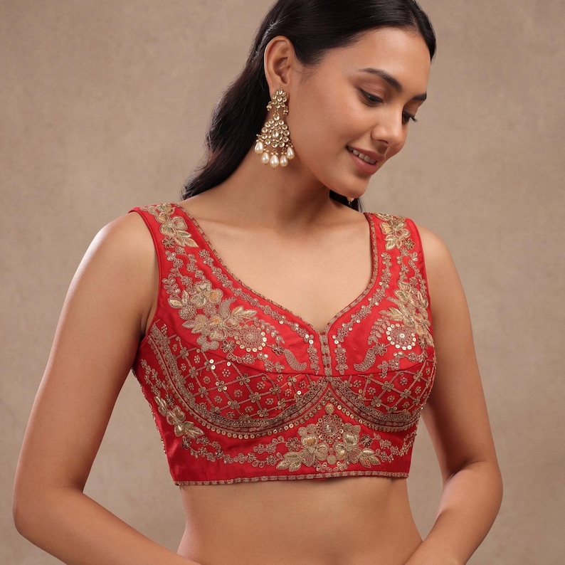 Op de afbeelding: Een mouwloze rode blouse met ingewikkelde gouden borduursels en pailletten. De blouse heeft een diepe V-hals en bloempatronen. Het kledingstuk is ontworpen voor formele gelegenheden.