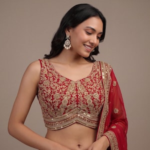Può includere: Una blusa rossa senza maniche con intricati ricami dorati e dettagli di paillettes su tutto il corpetto. Il capo presenta un orlo a forma di V ed è abbinato a una dupatta rossa trasparente coordinata con un bordo decorativo ricamato in oro.