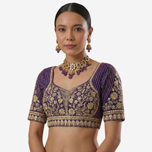 May include: A purple blouse with gold embroidery and a matching necklace and earrings. The blouse features intricate floral patterns and a square neckline. The jewelry includes purple gemstones. The overall style is elegant and ornate.