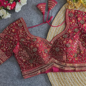 May include: A maroon embroidered blouse with gold sequin and bead embellishments. The blouse has a scoop neckline, three-quarter sleeves, and decorative tassels. This garment is likely intended for formal events or special occasions.
