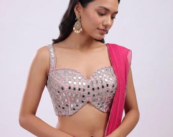Puede incluir: Un top rosa estilo bustier con adornos de espejos cuadrados. El top tiene tirantes anchos y un escote corazón. Una bufanda rosa a juego está drapeada sobre el hombro. El conjunto se completa con una falda rosa.