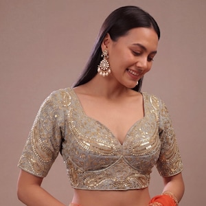 May include: A light gray blouse featuring intricate gold embroidery and sequin detailing in a paisley pattern. The garment has a sweetheart neckline, short sleeves, and a structured bodice design with heavy embellishments throughout the fabric.