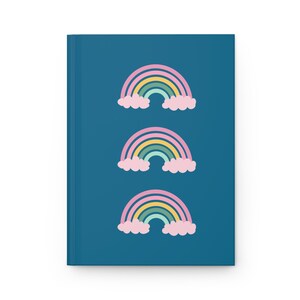 May include: A teal notebook with three rainbow illustrations. Each rainbow has a yellow, green, and blue arch with pink clouds at the base. The notebook is rectangular and has a clean, minimalist design.