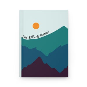 May include: A journal with a mountain landscape design. The cover features a teal and navy mountain range under a light blue sky with an orange sun. The text "Just getting started" is printed on the cover.