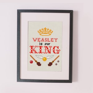 Pode incluir: Um desenho de ponto cruz enquadrado com uma coroa dourada, o texto "WEASLEY is our KING" em vermelho e duas snitches douradas com vassouras.