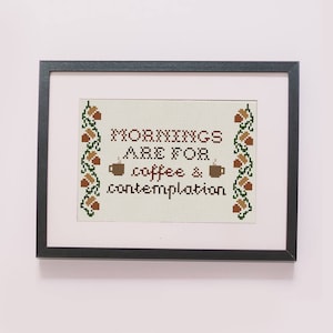 May include: A framed cross-stitch design with the text "Mornings are for coffee & contemplation" surrounded by a border of acorns and leaves.