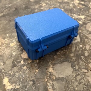 May include: A vibrant blue, rectangular, hard-shell case with a textured surface. The case features a secure latching mechanism, designed for protection. It is on a grey and brown marble surface.