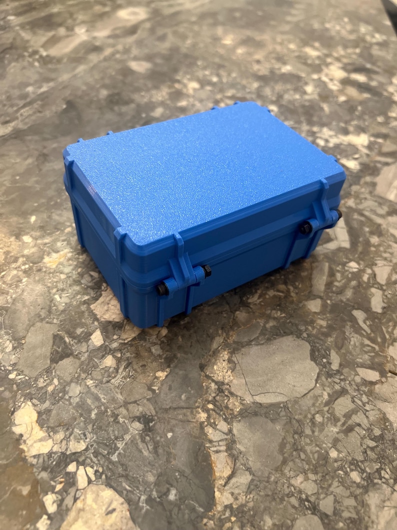 May include: A vibrant blue, rectangular, hard-shell case with a textured surface. The case features a secure latching mechanism, designed for protection. It is on a grey and brown marble surface.