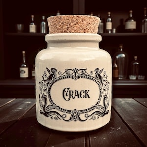 May include: A cream ceramic jar with a cork stopper. The jar has a black ornate design and the word "CRACK". The background includes a dark wooden surface and a shelf with bottles.