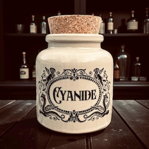 May include: A cream ceramic jar with a cork stopper, labelled "CYANIDE" in a decorative black oval. The jar has ornate black embellishments and is set against a dark background with bottles.