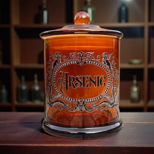 May include: An amber glass apothecary jar with a lid. The jar features a decorative label with the word "Arsenic" in ornate lettering. The jar is on a dark wooden surface.
