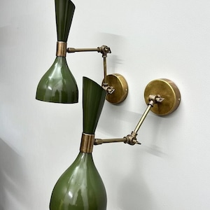 Könnte beinhalten: Zwei olivgrüne Wandleuchten mit Messingakzenten. Jede Leuchte hat einen konischen Schirm und einen verstellbaren Arm. Die Leuchten sind auf runden Messing-Rückplatten montiert und bieten eine Vintage-Ästhetik. Das Design ist elegant und modern.