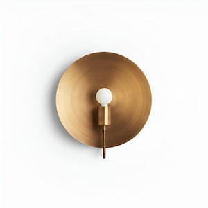 以下が含まれることがあります： 真鍮製のウォールスコンス。大きな円形のバックプレートと小さな円筒形の照明器具が特徴です。電球は白くて丸いです。スコンスは真鍮製で、暖かくメタリックな仕上がりです。