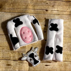 May include: A white cow costume set with black spots, including a long-sleeved shirt with a pink belly, pants, and a cow head. The costume is made of soft fabric and is designed for children.