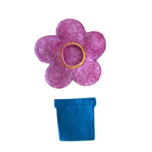 May include: A felt flower and pot set. The flower is a vibrant pink with a yellow center and white stitching. The pot is a solid blue square. The set is likely handmade and suitable for crafts or decoration.