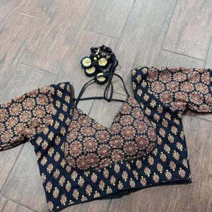 May include: A black and brown patterned top with short sleeves. The top features a floral design in shades of brown and gold. The top has a halter neck and a matching tassel detail.