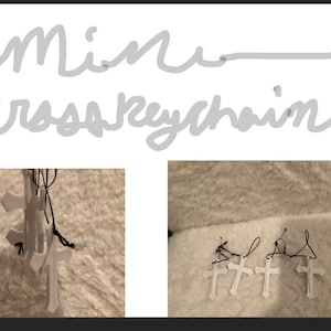 May include: White cross keychains with black cords. The image shows multiple keychains, some grouped together. The text "Mini cross keychain" is written in cursive at the top of the image.