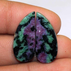 May include: Two polished teardrop-shaped gemstones. Each stone features a vibrant mix of colors: deep red, forest green, and black. The gemstones are cut in half, showcasing their unique patterns and textures. Ideal for jewelry making or collecting.
