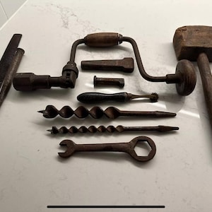 May include: A collection of antique woodworking tools, including a brace and bit, hammer, files, and a wrench. The tools are made of metal and wood, with a rustic, aged appearance. The arrangement suggests a focus on craftsmanship and vintage tools.