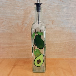 May include: A clear glass bottle with a black and silver pour spout. The bottle is decorated with hand-painted green avocados.