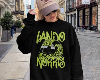 Może przedstawiać: Czarna bluza z długim rękawem z limonkową grafiką kasku wyścigowego z czarnym wizjerem oraz napisem Lando Norris stylizowaną czcionką. Ubiór uzupełnia beżowo-brązowa czapka z daszkiem z napisem The Western House Casino.
