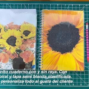 Puede incluir: Dos cuadernos con espiral con diseños florales, uno con girasoles y el otro con un gran girasol. Dos lápices y un bolígrafo están junto a los cuadernos. Los cuadernos están sobre una esterilla de corte verde.