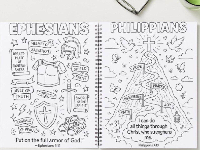 May include: A colouring book open at two pages with black and white drawings. One page shows the word "Ephesians" and armour elements. The other page has "Philippians" with a mountain and inspirational words.