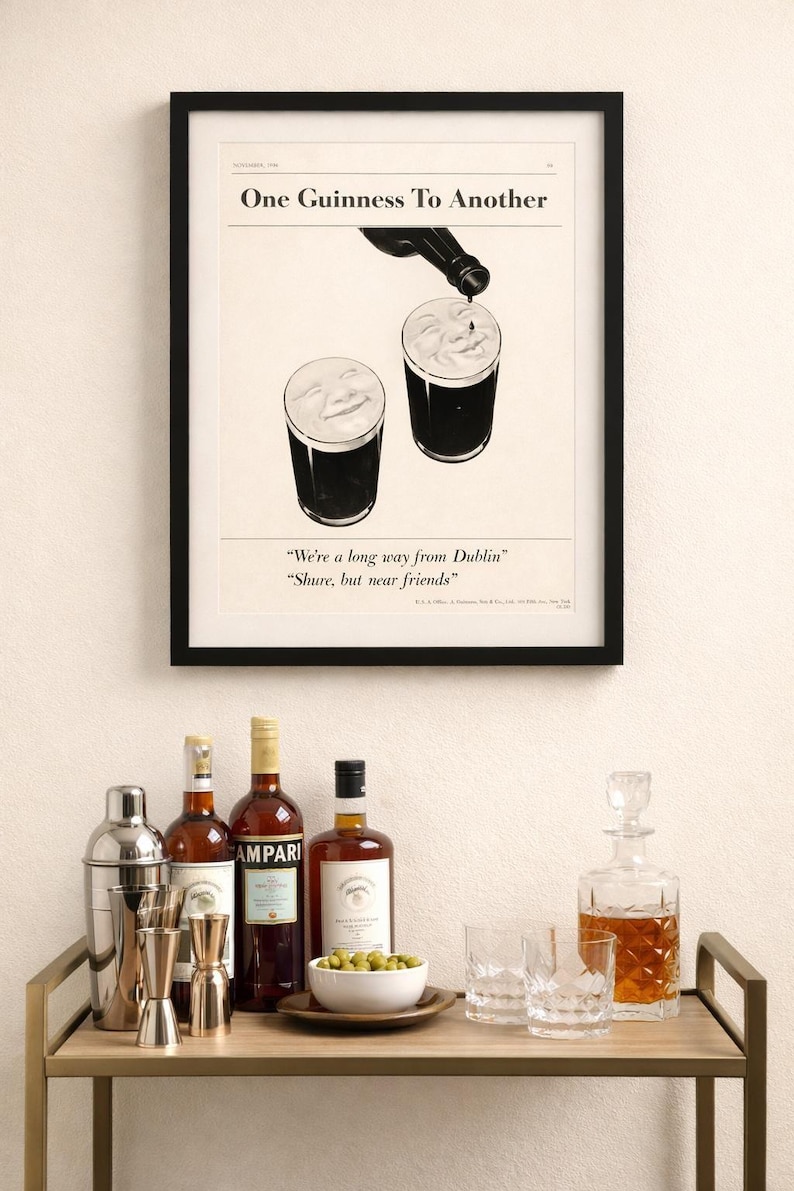May include: A framed print with the text "One Guinness To Another" above two glasses of stout. Below, a bar cart holds bottles of liquor, a cocktail shaker, jiggers, a bowl of olives, and glassware. A decanter is also present.