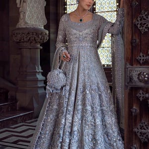May include: A silver-gray, floor-length gown with intricate embroidery and long sleeves. The dress features a fitted bodice and a flowing skirt. A matching beaded purse and jewelry complete the elegant ensemble. The gown is suitable for formal events.