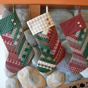 May include: Three Christmas stockings made of patchwork fabric with red, green, and white plaid patterns. Each stocking has two gold star buttons.