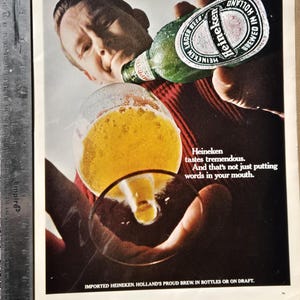Pu&ograve; includere: Pubblicit&agrave; vintage della birra Heineken. Un uomo beve da una bottiglia verde di Heineken, versandola in un bicchiere. Il testo recita: "Heineken ha un sapore tremendo. E non &egrave; solo mettere parole in bocca".
