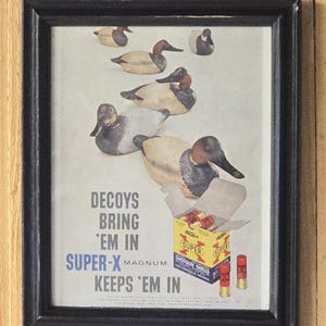 May include: Framed vintage advertisement featuring duck decoys and a box of Super-X Magnum shotgun shells. The text reads "Decoys Bring 'Em In, Super-X Magnum Keeps 'Em In."