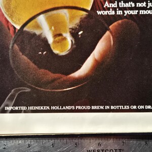 Pu&ograve; includere: Una pubblicit&agrave; che mostra birra versata in un bicchiere. L'immagine si concentra su una mano che tiene il bicchiere, con la birra che vi scorre dentro. Il testo in basso recita: "IMPORTED HEINEKEN. HOLLAND'S PROUD BREW. IN BOTTLES OR ON DRAFT."