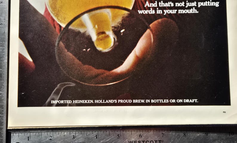 Pu&ograve; includere: Una pubblicit&agrave; che mostra birra versata in un bicchiere. L'immagine si concentra su una mano che tiene il bicchiere, con la birra che vi scorre dentro. Il testo in basso recita: "IMPORTED HEINEKEN. HOLLAND'S PROUD BREW. IN BOTTLES OR ON DRAFT."