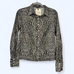 May include: A long-sleeved button-down shirt featuring a dark brown and light gray snakeskin print pattern. The shirt has a standard collar, a front button placket, and cuffs with three buttons each. A beige tag with the handwritten text 34B is attached.