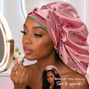 Puede incluir: Un gorro de satén rosa con detalles de estrellas verdes. El gorro está atado con un lazo y tiene un ribete verde. La imagen también incluye una pequeña imagen de una mujer que lleva un gorro más pequeño con el texto "BONNET TOO SMALL? Time to upgrade!"