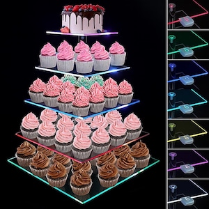 May include: A multi-tiered dessert stand with a chocolate cake and cupcakes. The cake is topped with berries. Cupcakes with pink and green icing are arranged on the clear, square shelves. The stand has colour-changing LED lights.