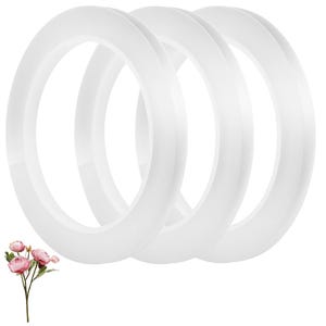 May include: Three translucent white rings are stacked together. The rings have a smooth, rounded shape. A sprig of pink flowers with green stems and leaves is in the lower left corner.