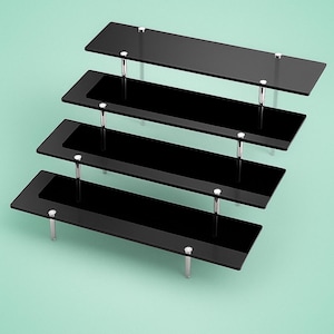 May include: A tiered display stand with four rectangular black shelves. The shelves are supported by silver-colored metal posts. The stand is designed to showcase items and is set against a light green background.