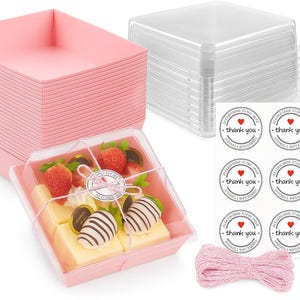 Op de afbeelding: Een set roze vierkante voedselcontainers met doorzichtige deksels, een stapel doorzichtige deksels en "bedankt" stickers. Eén container bevat desserts met aardbeien en chocolade. Roze touw is ook inbegrepen.