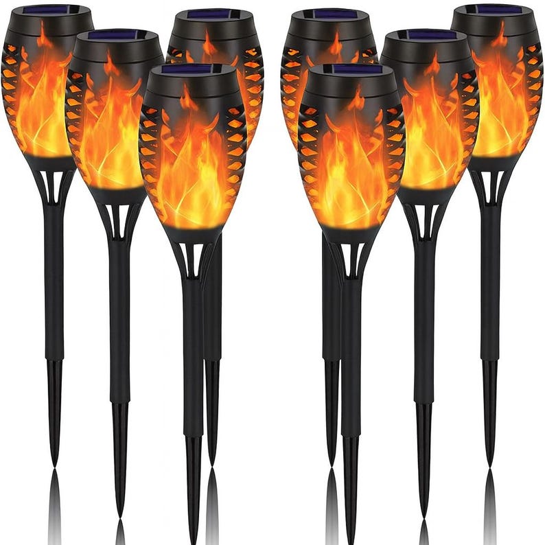 May include: A set of eight black solar-powered torches with a flame effect. The torches have a black stake for ground placement and a decorative cage around the flame. The torches are designed for outdoor use.