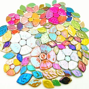 May include: A circular arrangement of glossy ceramic tiles in flower and leaf shapes. The tiles are in various colours, including pink, orange, yellow, blue, and green. The arrangement resembles a floral mosaic, with each tile having a glossy finish.