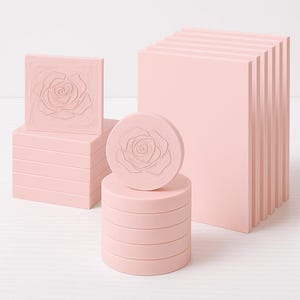 Op de afbeelding: Een verzameling roze decoratieve objecten, waaronder een vierkant blok met een rozenontwerp, een stapel gelaagde blokken, een ronde schijf met een roos en een rechthoekig blok. Het rozenontwerp is in reliëf.