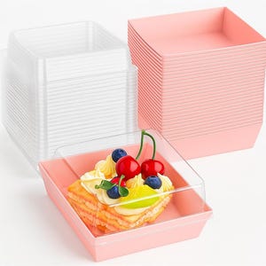 Puede incluir: Un conjunto de recipientes cuadrados rosas y transparentes apilados. Uno de ellos contiene un pastel decorado con cerezas y arándanos. Ideal para el almacenamiento y la presentación de alimentos.