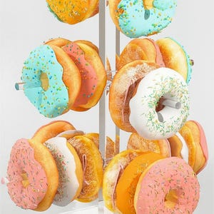 Puede incluir: Un expositor de donuts de acrílico transparente que contiene una variedad de donuts coloridos. Los donuts tienen diferentes glaseados y chispas, incluyendo naranja, azul, rosa y blanco. El expositor está sobre una superficie blanca.