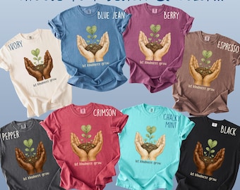 May include: Seven short-sleeved t-shirts in ivory, blue jean, berry, espresso, pepper, crimson, chalky mint, and black. Each shirt features a graphic of hands holding soil with a heart-shaped plant and the text "let kindness grow".