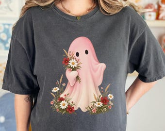 May include: A charcoal gray short-sleeve t-shirt featuring a central graphic of a light pink ghost holding a bouquet of white and red flowers. Additional white and red flowers and green foliage are positioned at the base of the ghost figure.