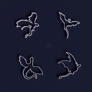 Puede incluir: Cuatro cortadores de galletas blancos con forma de dragón sobre un fondo azul oscuro. Cada cortador presenta una pose de dragón diferente, con alas extendidas y colas rizadas. Ideal para repostería.