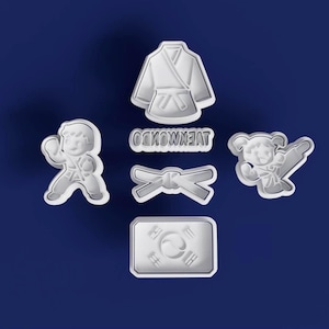 May include: A collection of white plastic cookie cutters in the shape of Taekwondo-themed designs. The set includes a uniform, belt, two figures in action poses, the Korean flag, and the word TAEKWONDO.